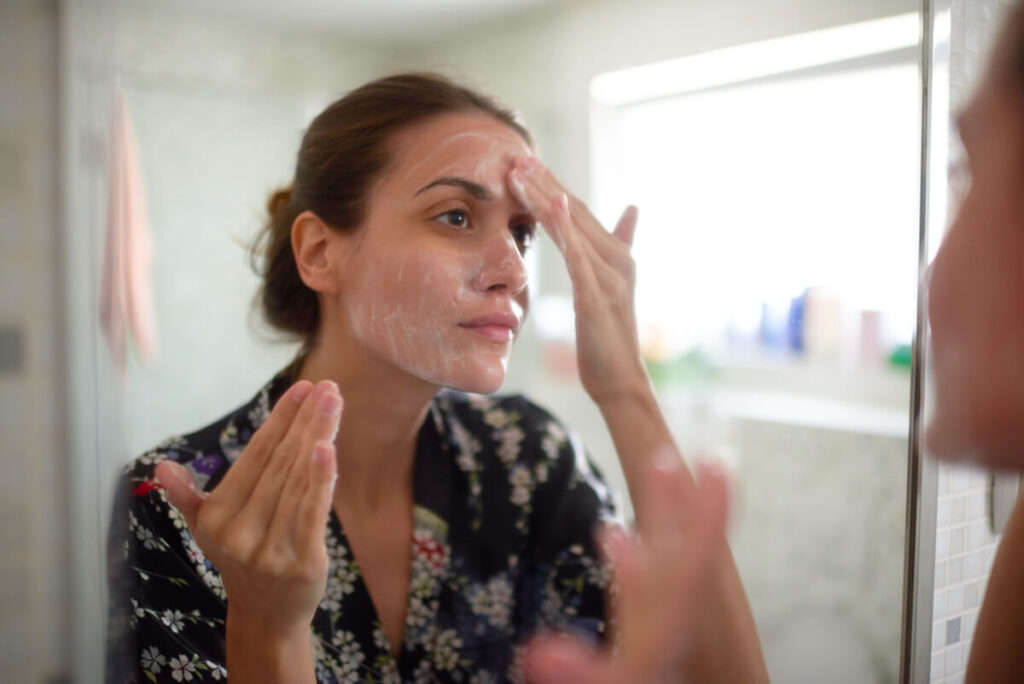 Young female in the bathroom looking in the mirror and taking care of her facial skin